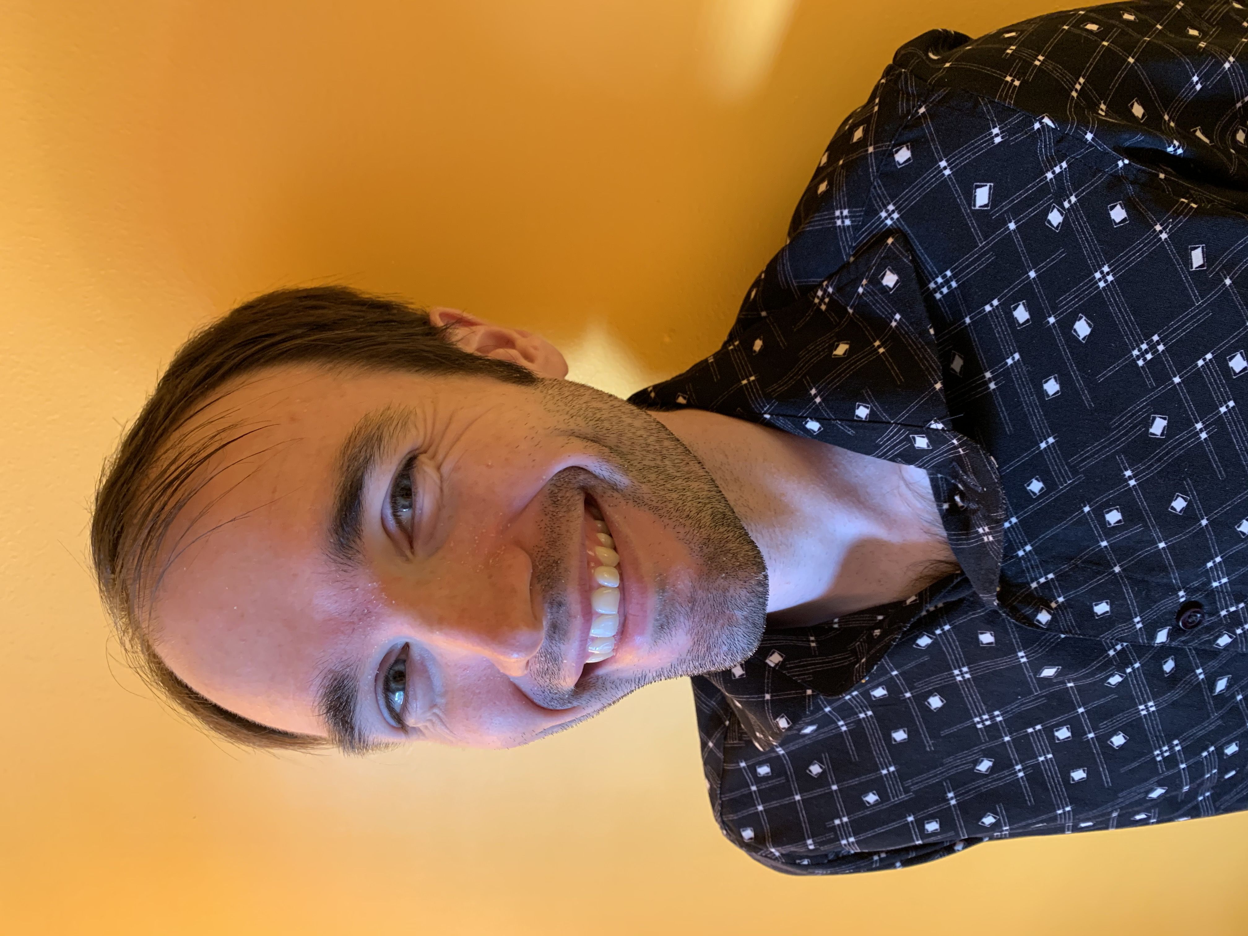 Taylor Robertson, front-end web developer, in a black collared shirt against an orange-yellow wall.